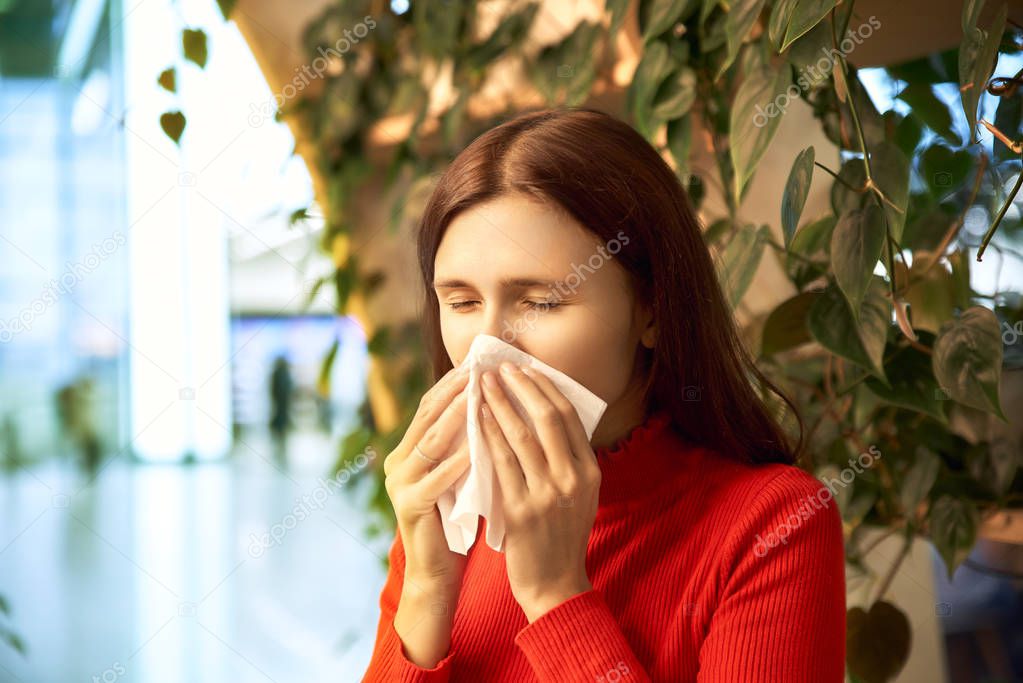 A frustrated woman sneezes due to allergies at the Mall. The concept of spring exacerbation of allergies, runny nose, colds