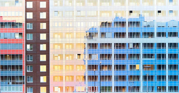 Textura horizontal de fachada azul de un enorme rascacielos residencial con un patrón regular de muchas ventanas que reflejan el sol de la noche. Un nuevo edificio moderno con muchas ventanas con reflejos de cielo azul —  Fotos de Stock