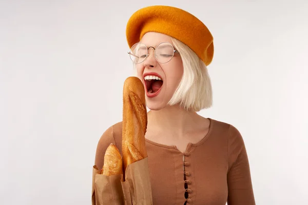 Porträt einer schönen jungen Frau, die Baguette in den Händen hält. fröhliche Frau in gelber Baskenmütze isoliert über weißem Hintergrund im Studio — Stockfoto