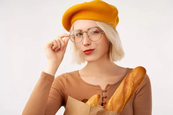 Портрет щасливої усміхненої жінки, що тримає паперовий мішок з довгим білим хлібом, з жовтим беретом та окулярами, коричневий піджак з красивими гудзиками — стокове фото