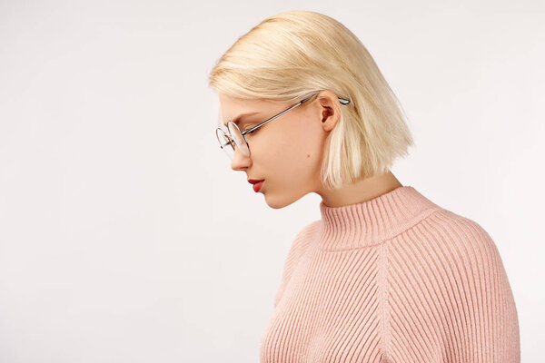 Profile of serious female with healthy pure skin, wears round glasses, has contemplative expression, isolated over white studio wall with copy space