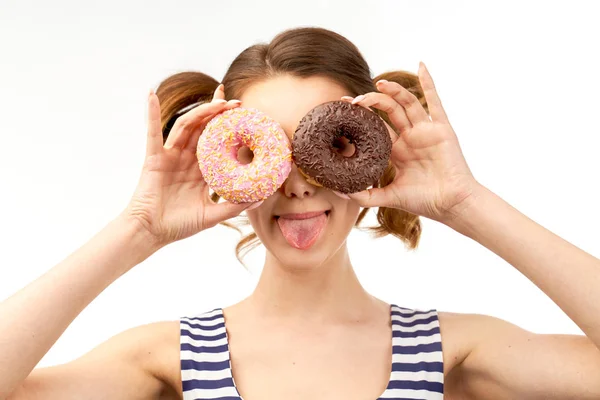 Attraktive junge Mädchen hält vor Augen glasierte Donuts und ein lustiges Lächeln zeigt die Zunge. Nahaufnahme Porträt auf isoliertem Hintergrund — Stockfoto