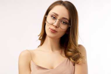 büyük yuvarlak gözlük çarpıcı genç kadın flörtöz gülümsüyor. Uzun koyu saçlı omuzlar etrafında kıvrılmış. Güzel sağlıklı cilt ve samimi ifade. İzole arka plan üzerinde büyük Studio portre