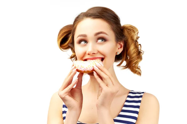 Ένα όμορφο κορίτσι με ένα κομψό χτένισμα δαγκώνει ένα ντόνατ και κλείνει τα μάτια της με ευχαρίστηση. Η έννοια των γλυκών, πρόχειρο φαγητό και ένα γρήγορο σνακ. Μεγάλο απομονωμένο πορτρέτο σε λευκό φόντο — Φωτογραφία Αρχείου
