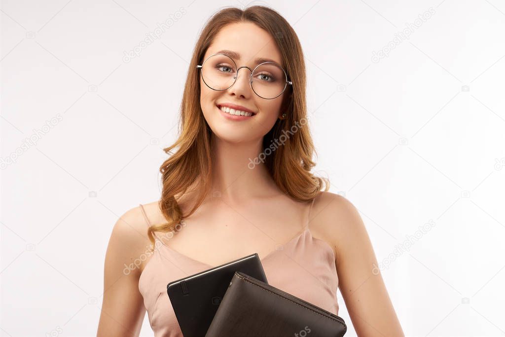 A pretty young woman student smiles charmingly and holds notebooks in her hands. Long curly dark hair and big round glasses