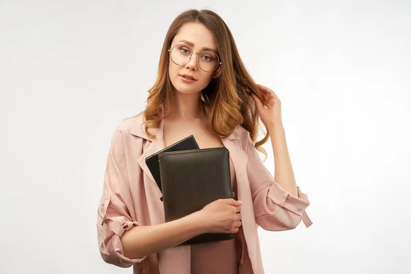 Business ung kvinna i en snygg kostym håller en anteckningsbok och ett sött leende. Den andra handen berör hennes långa lockiga mörka hår. Isolerat porträtt på vit bakgrund — Stockfoto