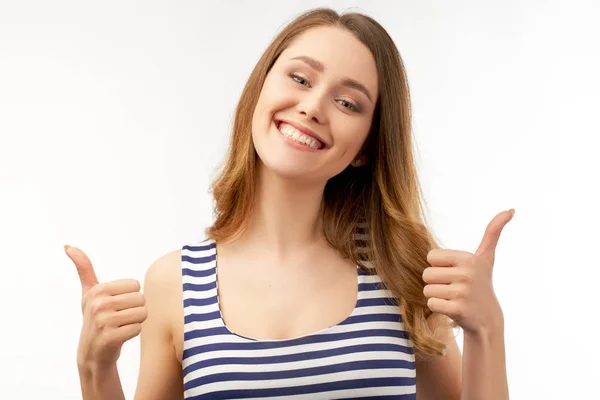En glädjefull lycklig tjej i en randig blå t-shirt visar ett tecken på tummen upp och ler brett. Långt lockigt mörkt hår. Stor Studio porträtt på isolerad vit bakgrund — Stockfoto
