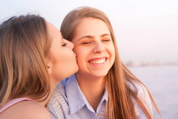 Piękna dziewczyna całuje siostrę, śmiech i bliskie oczy — Zdjęcie stockowe