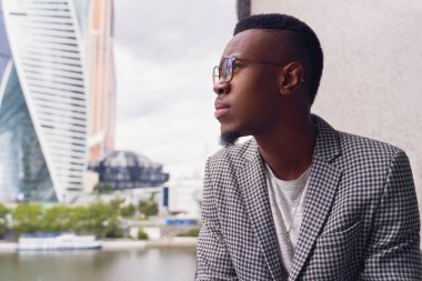 Genç koyu tenli adam düşünceli bir kenara bakıyor.