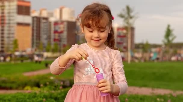 Lovely child blows soap bubbles on summer evening. — Stock Video
