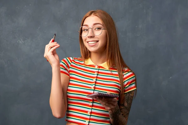 Дівчина тримає блокнот, ручка ізольована на текстурованій стіні — стокове фото