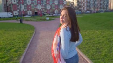 Kadın döndü, profili, nazik gülümsemesi, kameraya baktı, yarım yamalak, güzel gözlü. Güneşli bir videoda kadın gün batımında parkta yürürken görülüyor. Orta yaşlı esmer kız, rüzgar uzun siyah saçlar savuruyor.