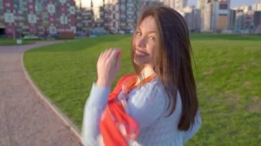 Kadın döndü, profili, nazik gülümsemesi, kameraya baktı, yarım yamalak, güzel gözlü. Güneşli bir videoda kadın gün batımında parkta yürürken görülüyor. Orta yaşlı esmer kız, rüzgar uzun siyah saçlar savuruyor.