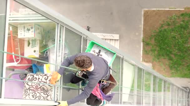 Vídeo do homem montanhista lavando janelas no edifício de vários andares. Profissão perigosa. A roupa de trabalho de tipo jovem cuidadosamente esfrega elementos de vidro de janela Brilha no alto crescimento, 6-6-19 Saint-Petersburg Rússia — Vídeo de Stock