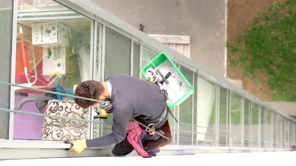 複数階建ての建物でWindowsを洗う登山家の男のビデオ。危険な職業だ。若い男の仕事の服を慎重に窓ガラスの要素を拭く輝きで高上昇、 6-6-19サンクトペテルブルクロシア — ストック動画