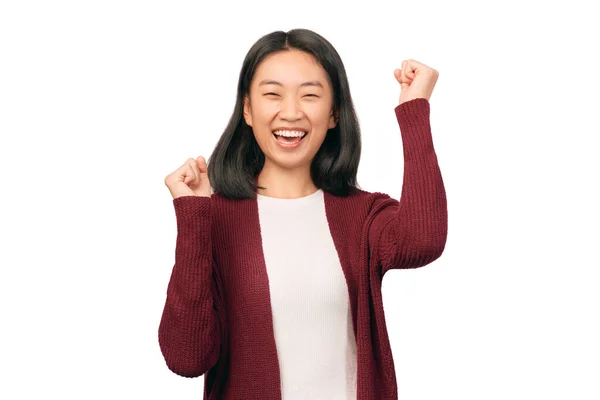 Fille gagnant de loterie célébrant heureusement sentir gagnant triomphant poings serrés victoire de succès. Belle femme d'apparence asiatique vêtue de cardigan bordeaux se tient isolé fond blanc Studio Photos De Stock Libres De Droits