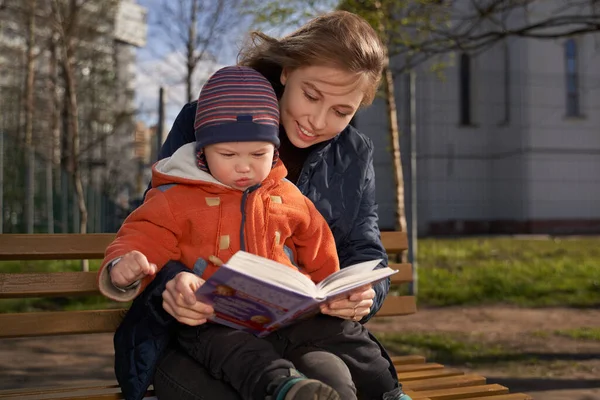 Une fille étreint un enfant, assis sur un banc, enfant sur les genoux des femmes, lire un livre, raconter une histoire Images De Stock Libres De Droits