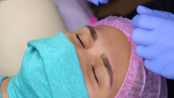 Belle jeune femme obtient procédure de correction des sourcils. épilation des sourcils. Fille couchée sur le canapé dans un salon de beauté. Soins du visage, visage de client en gros plan et mains de cosmétologue spécialiste. Vidéo 4K — Video