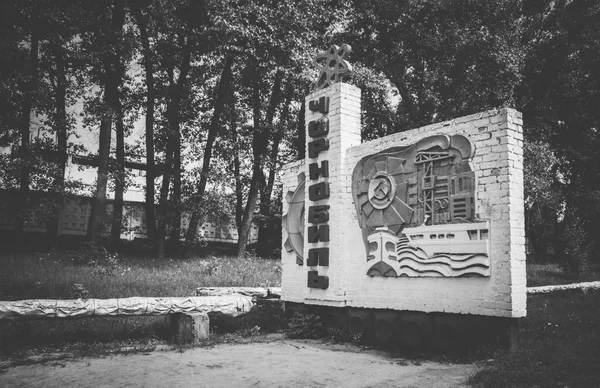 A black and white picture of the large town sign of Chernobyl in the main access road.