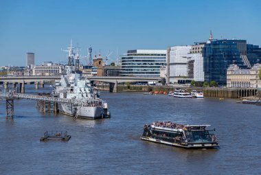 A picture of the HMS Belfast on the Thames, with a tourist cruise sailing next to it.