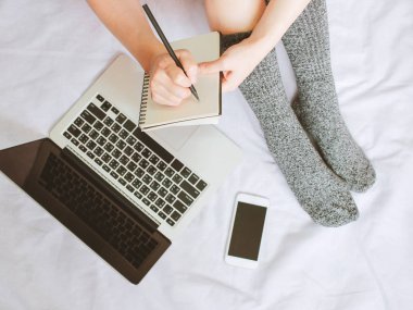 Kadın bacaklar çorap ve dizüstü dizüstü bilgisayar üzerinde yazma ve smartphone üstten görünüm rahat yatak, yaşam kavramı, sonbahar ve kış sezonu