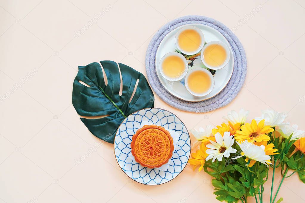 Top view of chinese moon cake with hot tea and flower on yellow background, holiday and festival concept