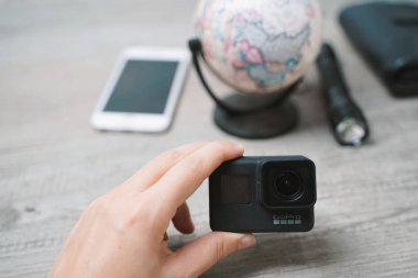 Bangkok, Tayland - 8 Ekim 2018: gezgin-blogger-fotoğrafçı için ahşap arka plan ayarlamak seyahat aksesuarları ile yeni Gopro Hero 7 siyah kamera tutan el.