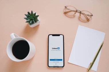 Ekran ve kahve bardağı üzerinde Linkedin uygulaması ile çalışma masası ve Apple iPhone XS düz yatıyordu