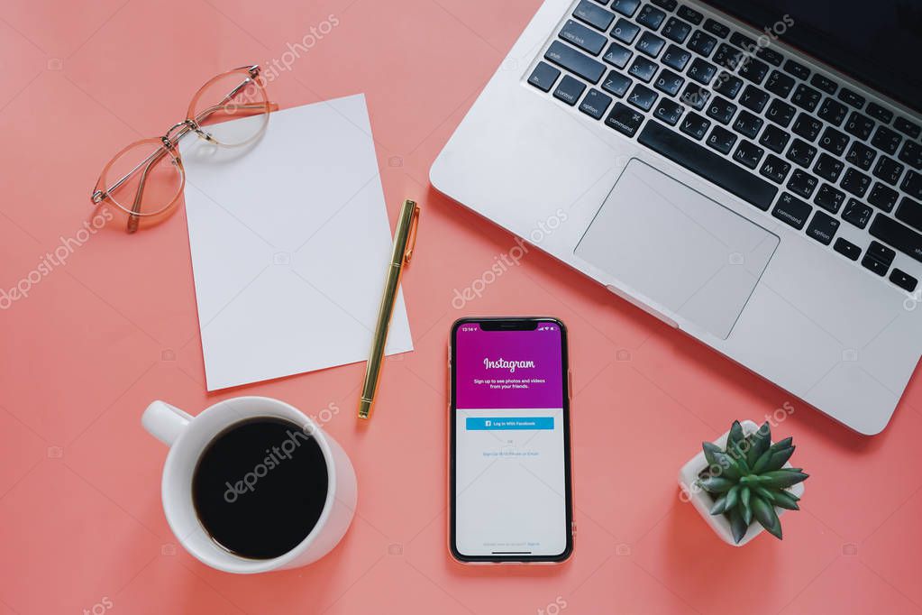 Flat lay workspace desk and Apple iPhone XS with Instagram application on screen with laptop and coffee cup on pink background