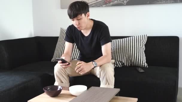 Jeune Homme Assis Sur Canapé Utilisant Télécommande Tout Mangeant Pomme — Video