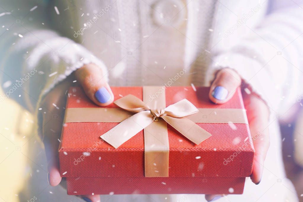 female hands in winter sweater holding red gift box for surprising in snow background, Merry Christmas concept