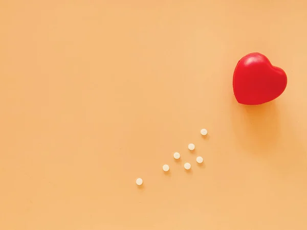 オレンジの背景に心臓の形と白い薬の丸薬のトップビュー 健康と医療の概念 — ストック写真