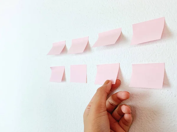 女性の手はオフィス ビジネス プレゼンテーションのアイデアで白い壁の背景に空白のピンクの付箋を選ぶ — ストック写真