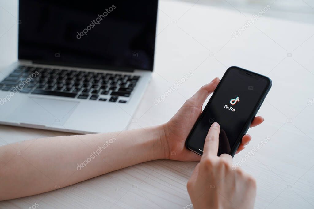 Nakhon Ratchasrima, Thailand - May 25, 2020 : woman using iPhone XS showing Tik Tok application on screen and laptop, Tik tok is popular social media network and entertainment
