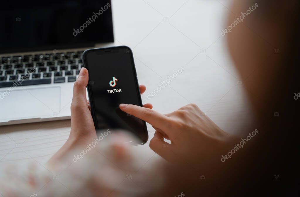 Nakhon Ratchasrima, Thailand - May 25, 2020 : woman using iPhone XS showing Tik Tok application on screen and laptop, Tik tok is popular social media network and entertainment