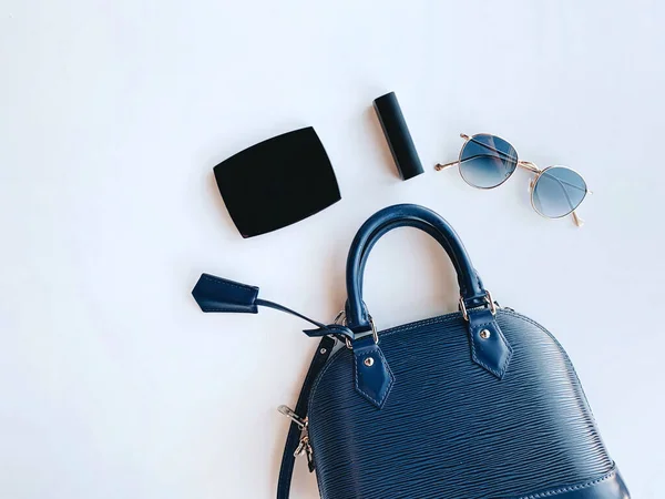 Flat lay of woman bag with cosmetics and sunglasses on white background with copy space, fashion and lifestyle concept