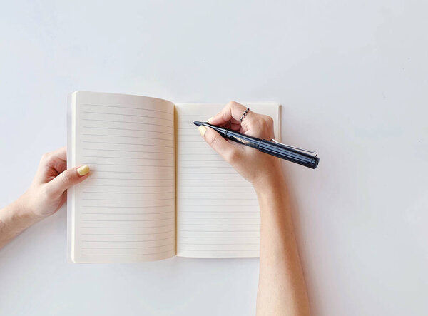 Top view of young woman writing on blank lined paper notebook on white table background, education or business concept