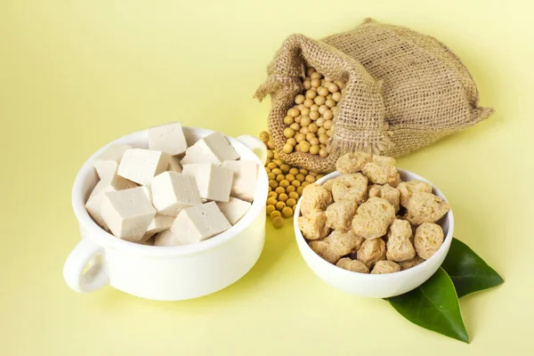 Organic soy products on light yellow background: soy beans, tofu and soy meat