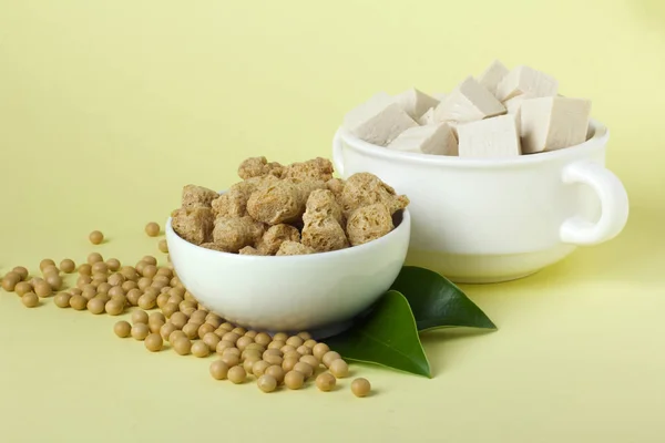 Organic soy products on light yellow background: soy beans, tofu and soy meat