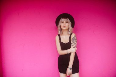 Güzel genç kadın dövme ve siyah elbise pembe duvara yakın poz ile