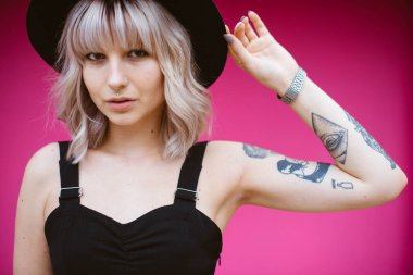 Güzel genç kadın dövme ve siyah elbise pembe duvara yakın poz ile