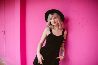 Güzel genç kadın dövme ve siyah elbise pembe duvara yakın poz ile