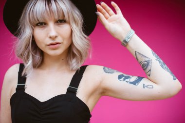 Güzel genç kadın dövme ve siyah elbise pembe duvara yakın poz ile