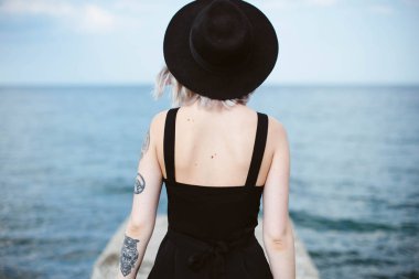 Güzel genç kadın dövme ve deniz arka plan üzerinde poz siyah elbise ile