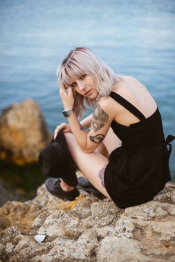 Güzel genç kadın dövme ve deniz arka plan üzerinde poz siyah elbise ile