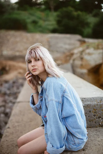 Taşlı sahilde denize sıfır kot ceket giyen güzel genç sarışın hippi kız. Açık havada