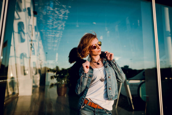 Beautiful fashion woman with  short hair  and make up posing in jeans on city street at sunset