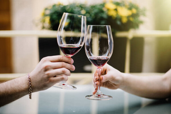 Cheers. Young loving couple sitting close to each other smiling and  toasting with two red wine glasses.