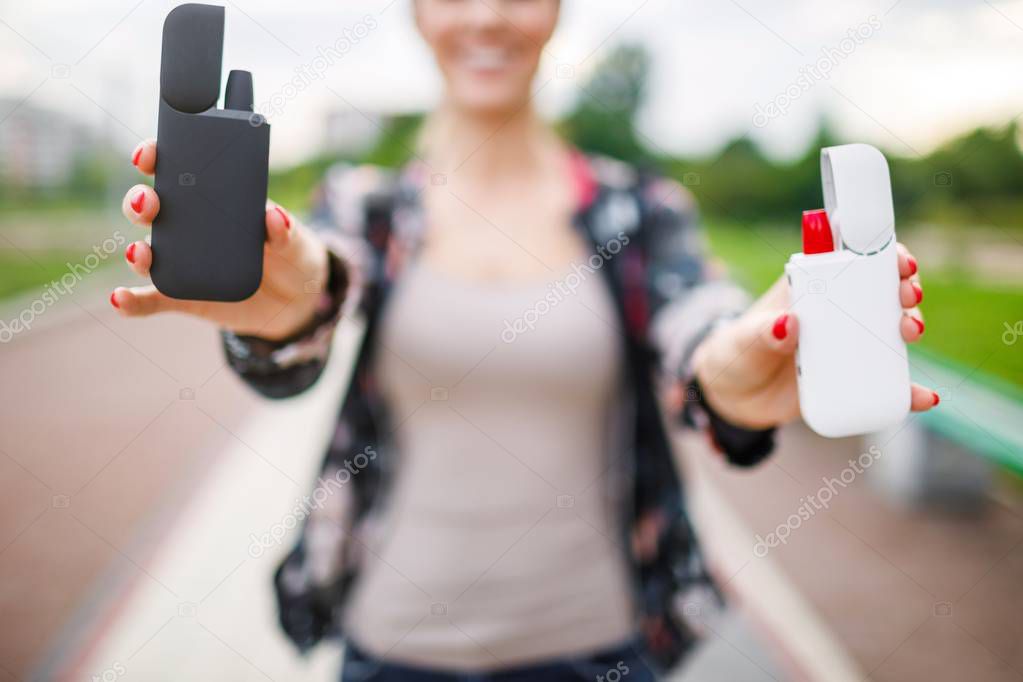 Close-up Of Woman Holding Electronic Cigarette In Hand.  Beautiful girl uses an electronic cigarette. Tobacco system IQOS.