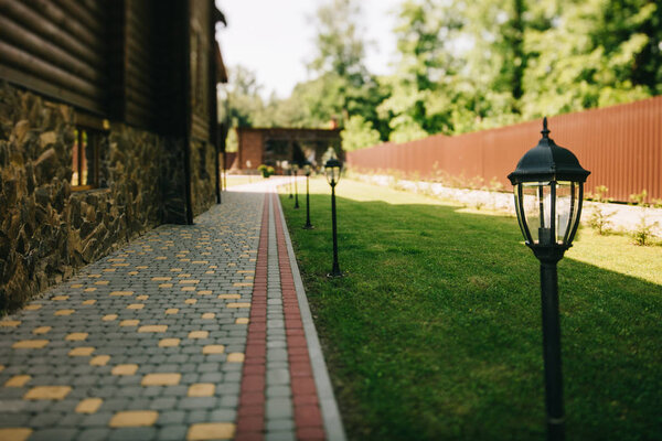 Уличные кованые металлические фонари на ухоженном коттедже с зеленой травой
 